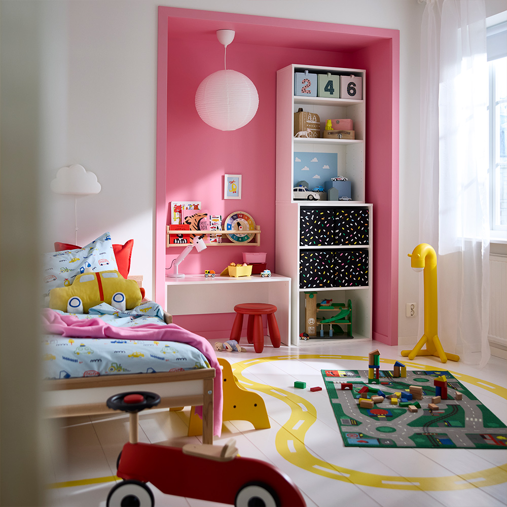 Una sala de juegos colorida con una combinación de armario LASTARE con cajas y juguetes en los estantes, junto a una cama y una zona de juego.