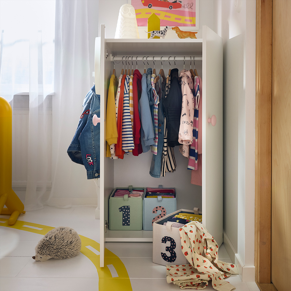 Ropa infantil colgada y cajas de almacenamiento etiquetadas en una combinación baja de armario LASTARE, ubicada en una habitación infantil luminosa.