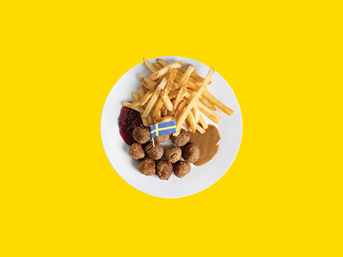 Plato con albóndigas suecas y papas fritas sobre fondo amarillo brillante.