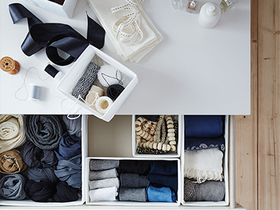 Top view of a white drawer organized with fabric boxes, folded clothes, and sewing supplies.
