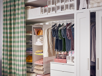 White closet system with hanging organizers, clothes on hangers, and green plaid curtain.