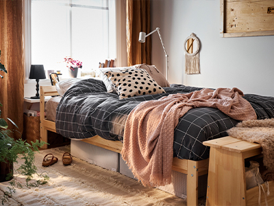 Wooden bed with dark grid duvet, pink throw blanket, and storage boxes underneath.