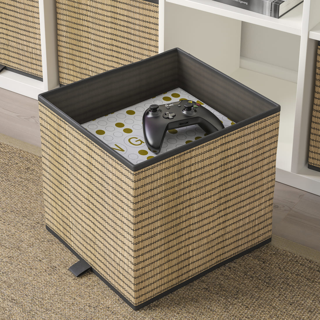 Woven natural fiber cube storage box with dark trim, containing a video game controller inside next to a white shelving unit.