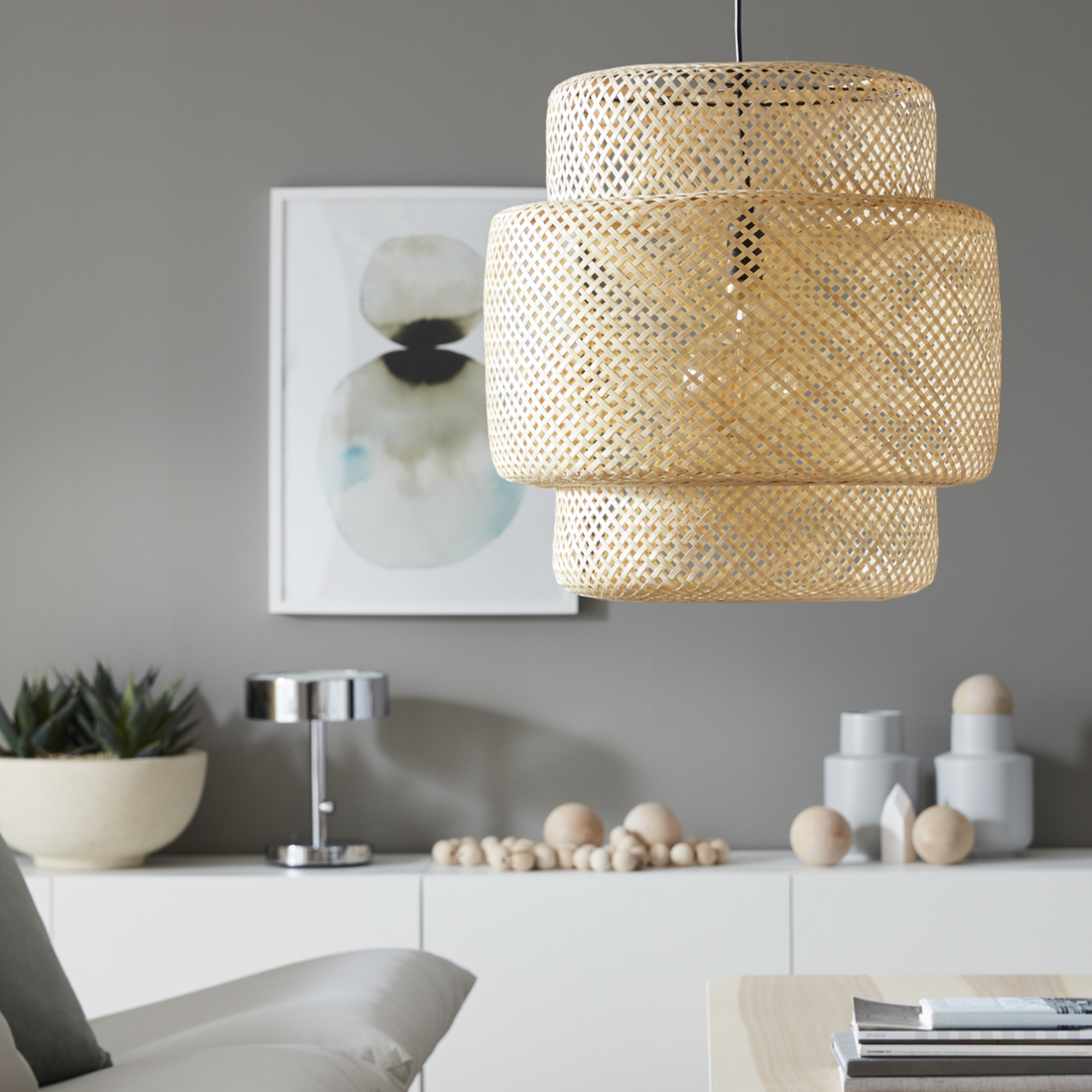 Three-tier woven bamboo pendant light hanging in a living room decorated with neutral tones and white furniture.
