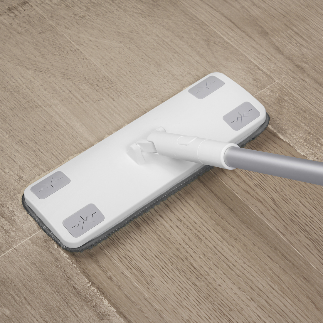 Mopa plana de limpieza blanca con almohadilla de microfibra gris deslizándose sobre un suelo de madera clara.