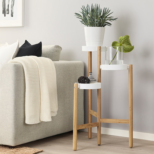 Moderno soporte de plantas de bambú y acero con macetas y jarrón, junto a un sofá gris.