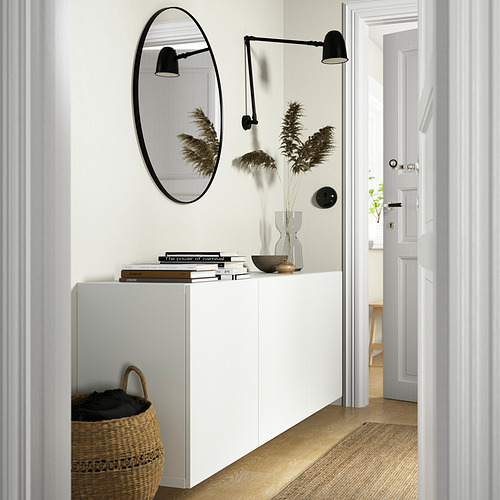 Mueble blanco BESTÅ, minimalista. Libros, cuenco, plantas secas. Parte superior del espejo, parte inferior de la cesta. Lámparas negras en los laterales.