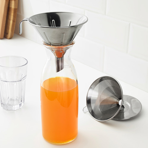 Jarra de vidrio con líquido naranja, filtro de metal en la parte superior, pieza de filtro adicional al lado.