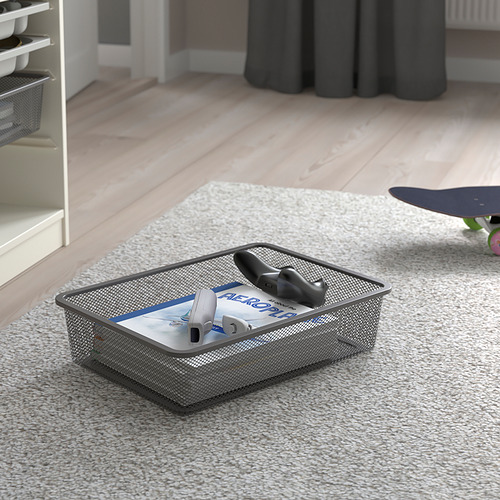Caja de almacenamiento de malla metálica sobre alfombra con controladores de juegos y estuche. Herramienta de organización TROFAST para un fácil acceso y orden.