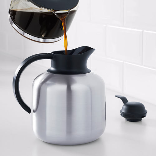 Frasco de vacío de plata con tapa y asa negras que se vierten con café de la jarra de vidrio.
