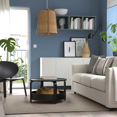 Sala de estar moderna con paredes azules, sofá blanco, mesa de centro negra, lámpara de mimbre, silla negra, plantas, estantería y gran ventanal.