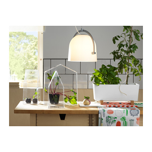 Cocina moderna con terrarios de plantas acrílicas transparentes sobre soportes de bambú, lámpara colgante blanca y mantel con estampados vegetales.
