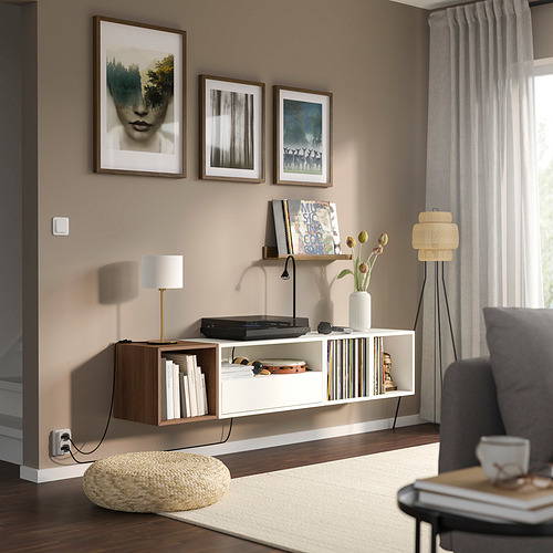 Sala de estar moderna con estante EKET, tocadiscos, libros, lámpara y arte. Sofá gris, lámpara de pie y visillos junto a la ventana.