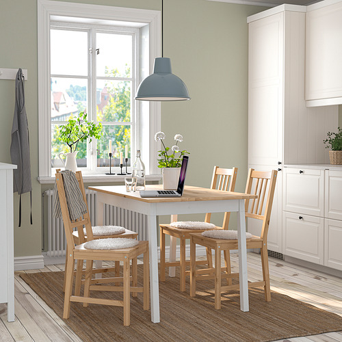 Acogedora cocina con mesa blanca, sillas de madera, lámpara azul, plantas y ventana.