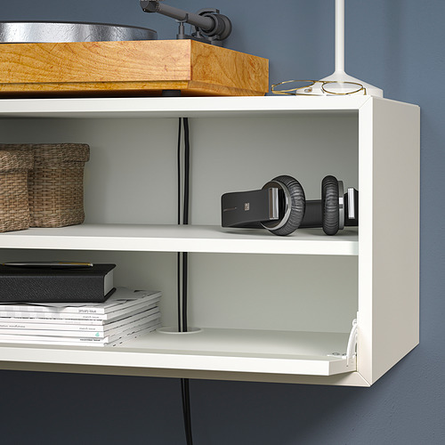 Una estantería blanca montada en la pared con cestas de almacenamiento, libros, auriculares y equipo de realidad virtual. Gestión de cables y un frente de apertura a presión.