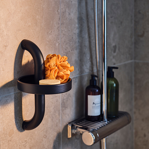 Soporte de ducha BÄSINGEN negro con esponja naranja y botellas de jabón, diseño moderno con acabado gris oscuro, montado sobre pared de azulejos grises.
