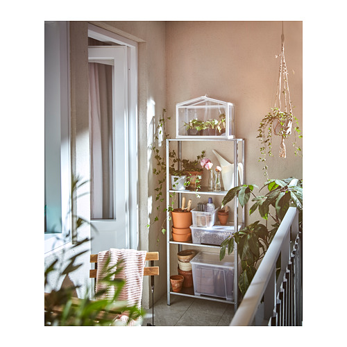 Estanterías HYLLIS con plantas y herramientas, pared beige, ventana con cortinas rosas, percha de macramé, silla con manta.