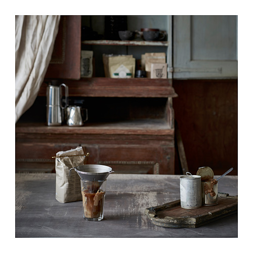 Cocina vintage con configuración de café, que incluye un filtro de café plateado, frijoles embolsados y recipientes con utensilios en una mesa de madera rústica.