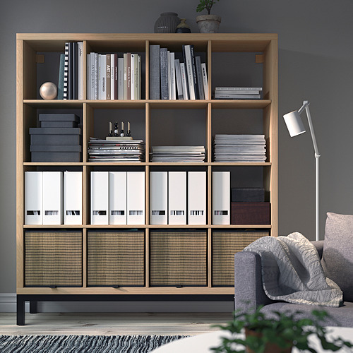 Estantería KALLAX con libros, archivos, decoración. Alto, junto a silla gris, paredes gris oscuro.