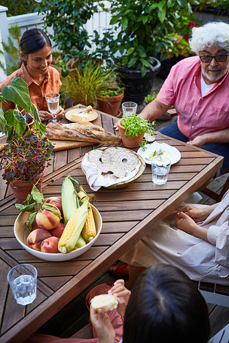 La familia disfruta de una comida al aire libre en la robusta mesa de acacia NORRMANSÖ, rodeada de exuberante vegetación.