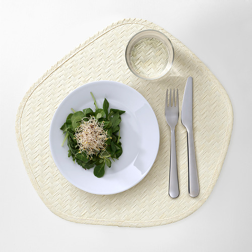 Plato blanco con ensalada verde sobre estera tejida. Insertado con tenedor y cuchillo, vaso pequeño.
