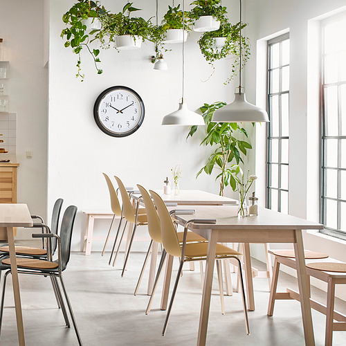 Cocina espaciosa y moderna con juego de comedor blanco, plantas y un reloj redondo silencioso con marco negro en la pared.