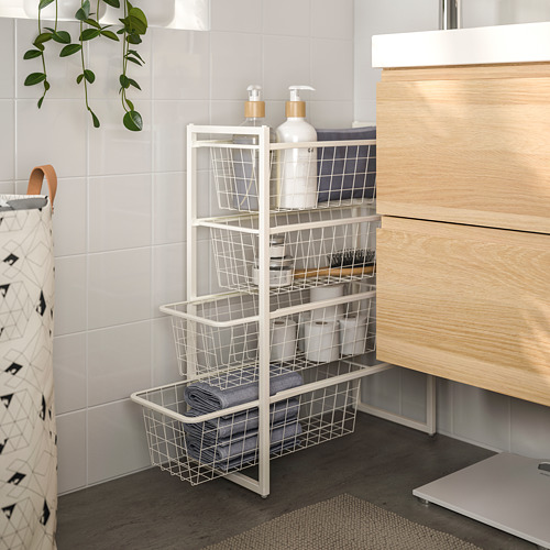 Mueble de baño de metal blanco JONAXEL con múltiples cestas, guardando ordenadamente botellas y toallas, situado entre la pared de azulejos y el tocador de madera.