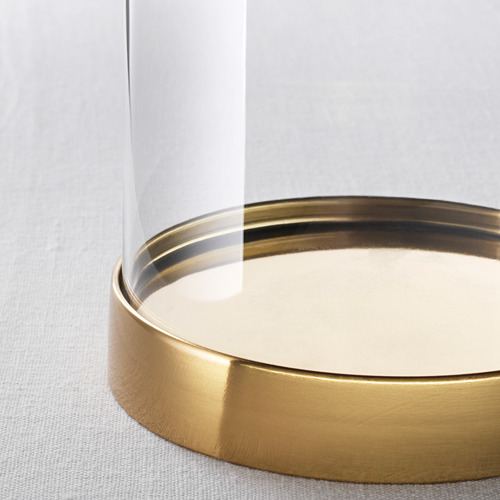 Primer plano de una elegante cúpula de vidrio transparente con una base metálica dorada, que refleja la luz, mostrando un elemento decorativo en su interior.