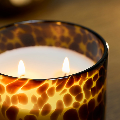 A lit candle in a patterned glass container, emitting a warm, inviting glow with three wicks, showcasing high-quality craftsmanship.