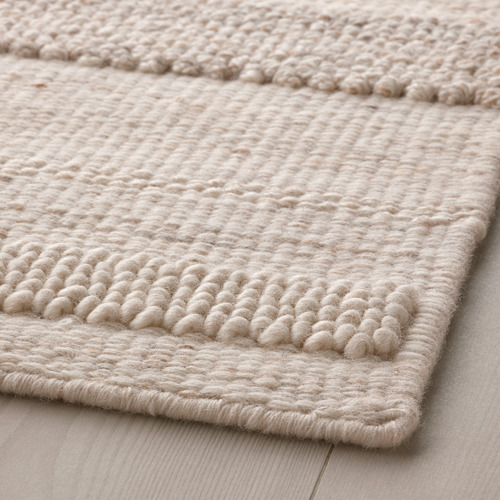 Alfombra de lana tejida a mano de color beige con variados patrones de texturas sobre suelo de madera.