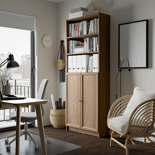 Librería BILLY en madera clara junto al escritorio, silla, cerca del balcón. Libros y decoración, se adapta a la habitación minimalista moderna.
