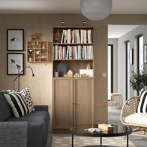 Moderno salón con librería Billy, sofá, silla de mimbre y lámpara de pie regulable.