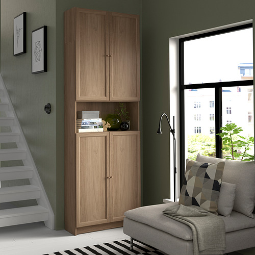 Habitación moderna con estantería alta de madera BILLY, sofá gris y gran ventana.