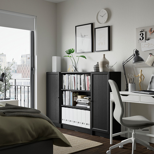 Sala de estar moderna con estantería BILLY de madera oscura, escritorio, cama y decoración.