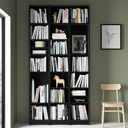 Estantería negra BILLY con libros, silla y arte de colibríes contra la pared verde.