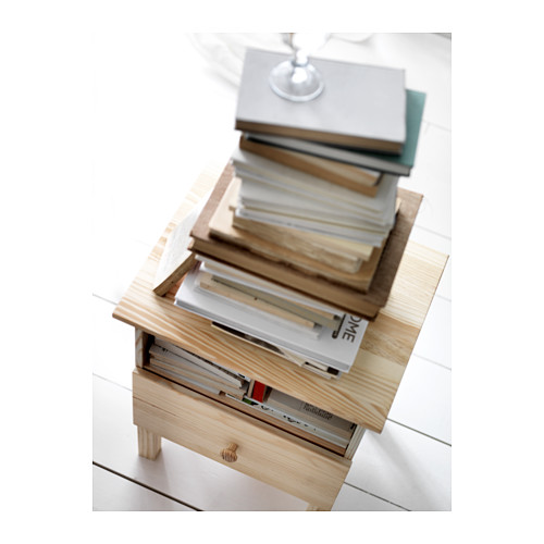 Mesita de noche de madera llamada TARVA. Libros apilados y un objeto de cristal en su superficie.