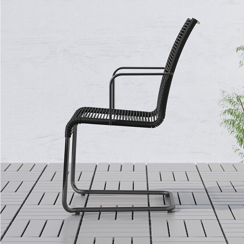 Silla de exterior moderna negra con respaldo alto y reposabrazos para mayor comodidad, colocada en un patio con baldosas.