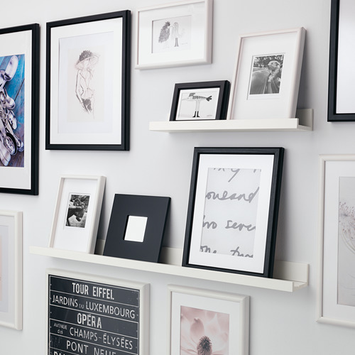 Estante de cuadros montado en la pared que muestra varias fotos y obras de arte enmarcadas, mostrando una mezcla de recuerdos y piezas decorativas.