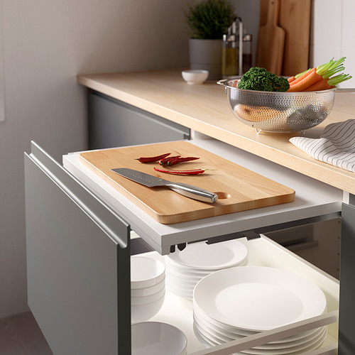 Tabla de cortar de madera extraíble en el cajón de la cocina, que se muestra con cuchillo y verduras.