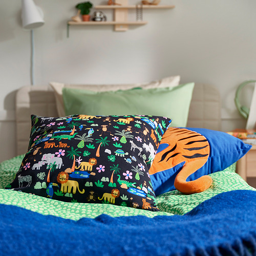 Almohadas de colores, edredón verde, cabecero blanco, planta, lámpara, estanterías.