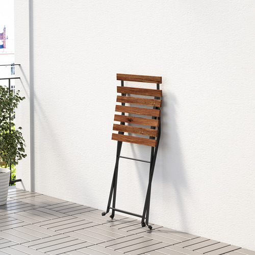 Silla plegable de madera con ruedas apoyada en la pared, apta para uso interior/exterior.