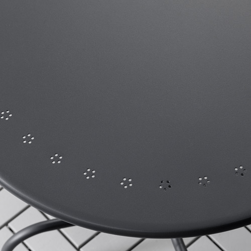 Moderna mesa redonda de exterior con tapa gris oscuro y base metálica, con pequeños motivos de estrellas.