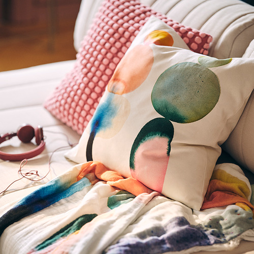 IKEA PS 2026: bright cushion on bed, patterned, squares & rounds. Size is small, next to large headphones.