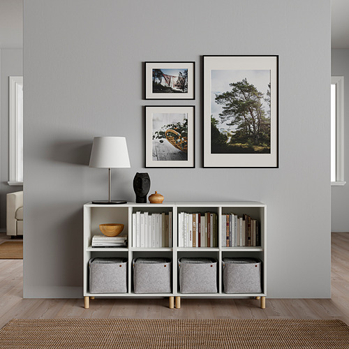 Sala de estar minimalista con almacenamiento EKET, lámpara de mesa y 3 fotos de la naturaleza enmarcadas.