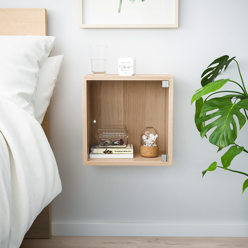 Dormitorio minimalista con estantería flotante de madera, decoración blanca y planta verde.
