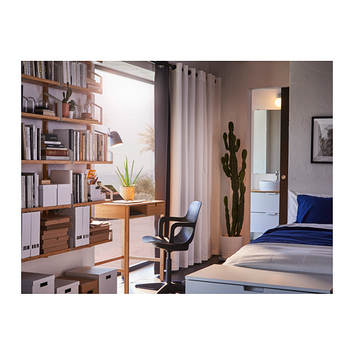 Acogedora habitación con cortinas grises, estanterías de madera, ropa de cama azul, escritorio, silla y grandes cactus.