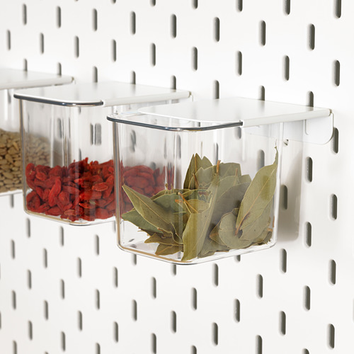 Las cajas de almacenamiento de plástico translúcido cuelgan de un tablero perforado blanco, con hierbas secas y especias. Ideal para la organización de la cocina y de fácil acceso.