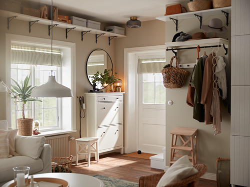 Sala de estar moderna con muebles blancos y estantes BERGSHULT que sostienen cestas y plantas. Paredes beige, suelos de madera, luz natural.