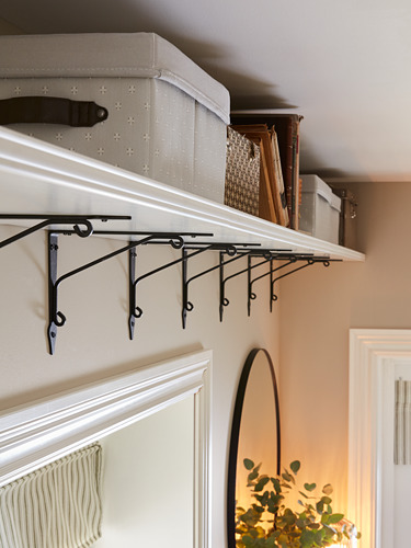 Estante de pared blanco con soportes negros, que contiene cajas de almacenamiento y libros. Espejo circular con planta debajo.