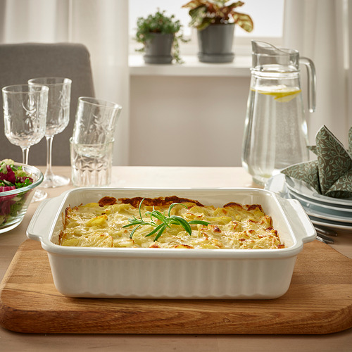 Plato de gratinado en la mesa, servido en una gran fuente de horno blanca con asas, acompañado de vasos y jarra.